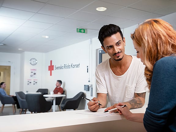 Två personer som har en dialog i receptionen på RKC i Malmö. Mannen står vänd mot fotografen och kvinnan står med ryggen mot fotografen.