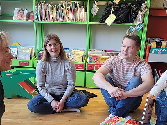 Föräldrarna Moa och Jens sitter på golvet och deras barn leker intill.