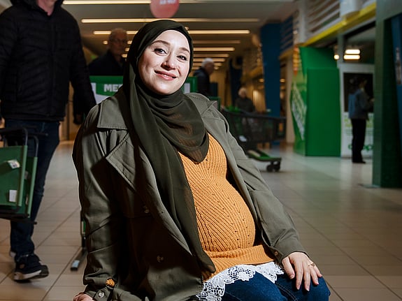 Rewa Almakhooth sitter på en bänk i ett köpcentrum och har en vinterjacka på sig. Runtomkring henne går människor.